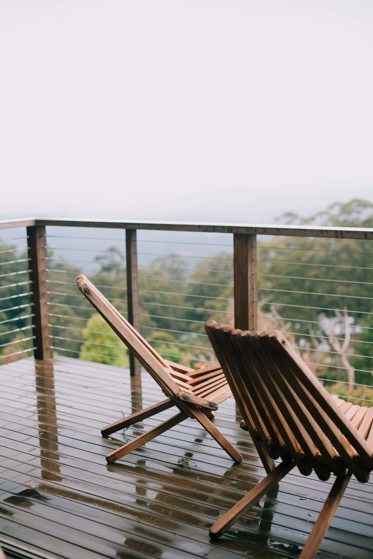 Hardwood deck with stainless cable railing and folding wood chairs overlooking treetops